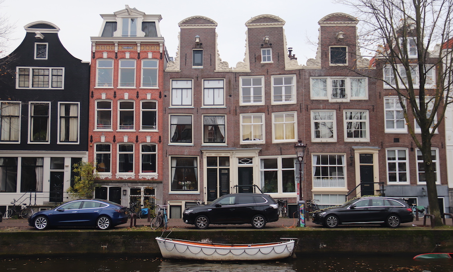 Cars park in front of crooked canal houses on the canal