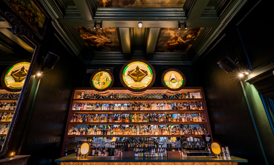 Dark bar at the Flying Dutchman cocktail bar in Amsterdam with a wall full of bottles for mixing good cocktails.