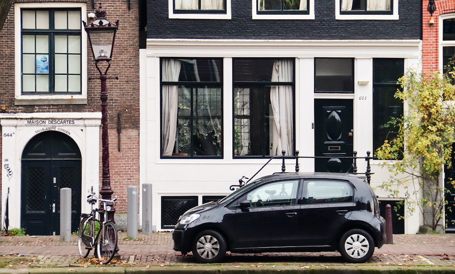 Black car parked in front of a black and white canal house