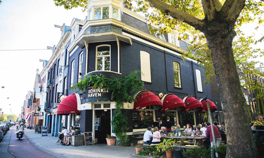 Guests sit in front of the black Café Schinkelhafen with red awnings